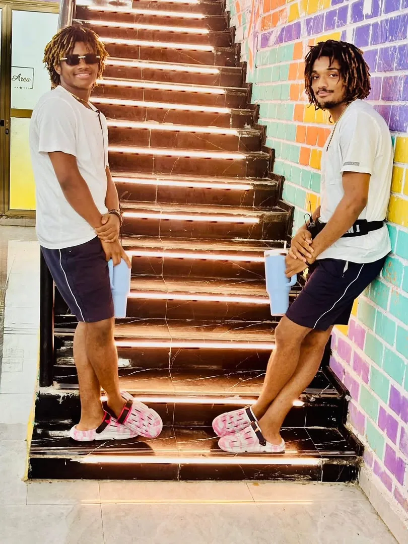 Jacob and Joseph Sesay together on a colorful staircase, brothers in white tees