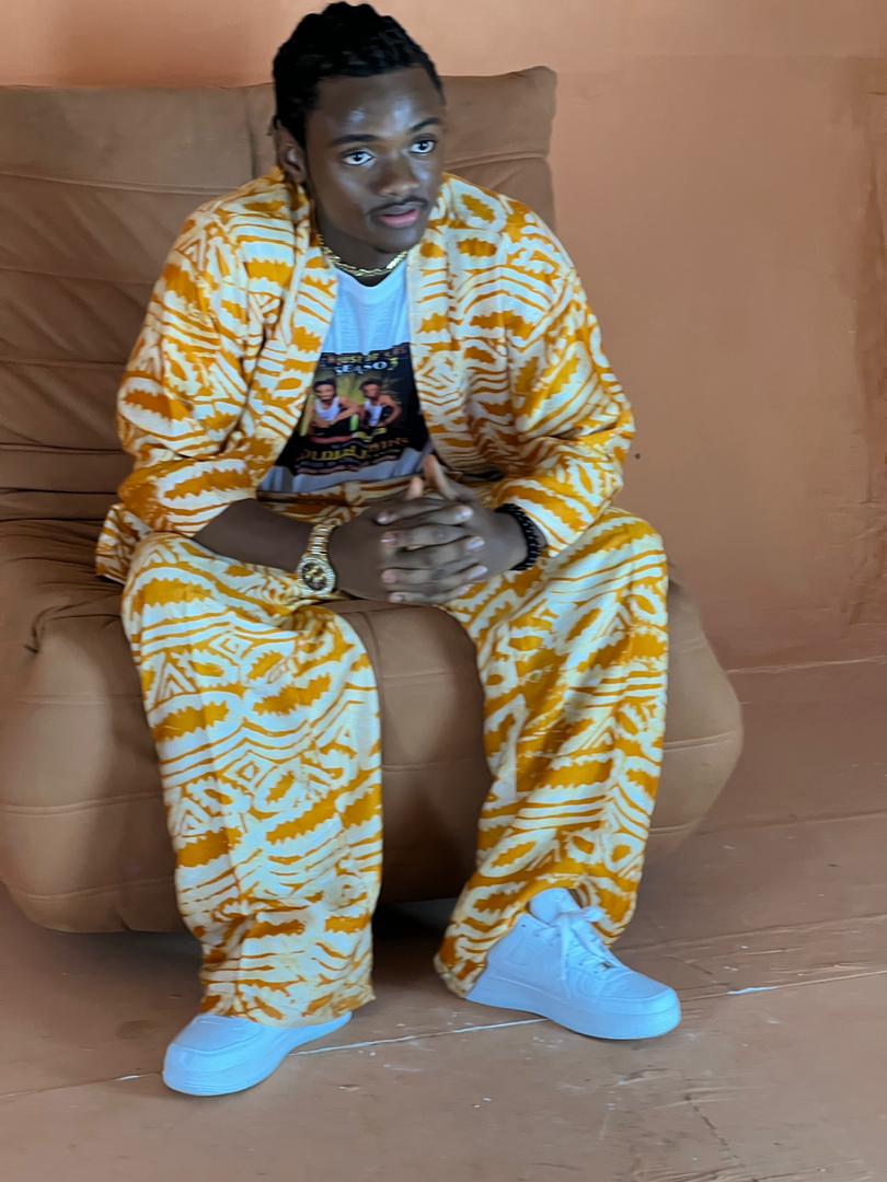 Jacob Sesay seated in a traditional gold-and-white outfit, replacement for the House of Stars campaign section