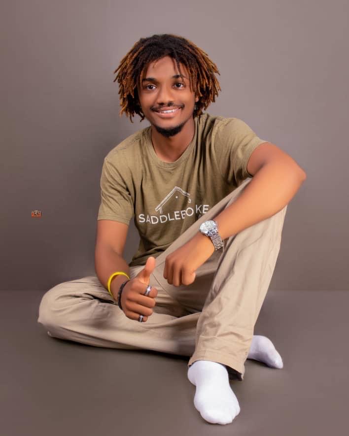 Jacob Sesay studio portrait in olive Saddlebok tee, thumbs-up