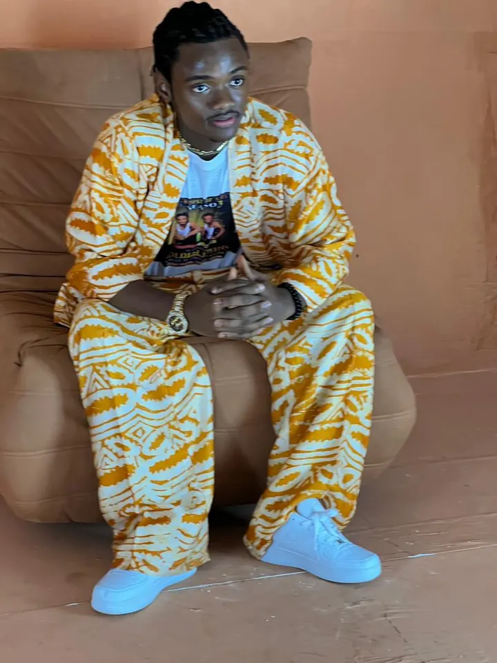 Jacob Sesay seated in a gold-and-white traditional outfit, House of Stars Season 3 tee, gold chain and watch