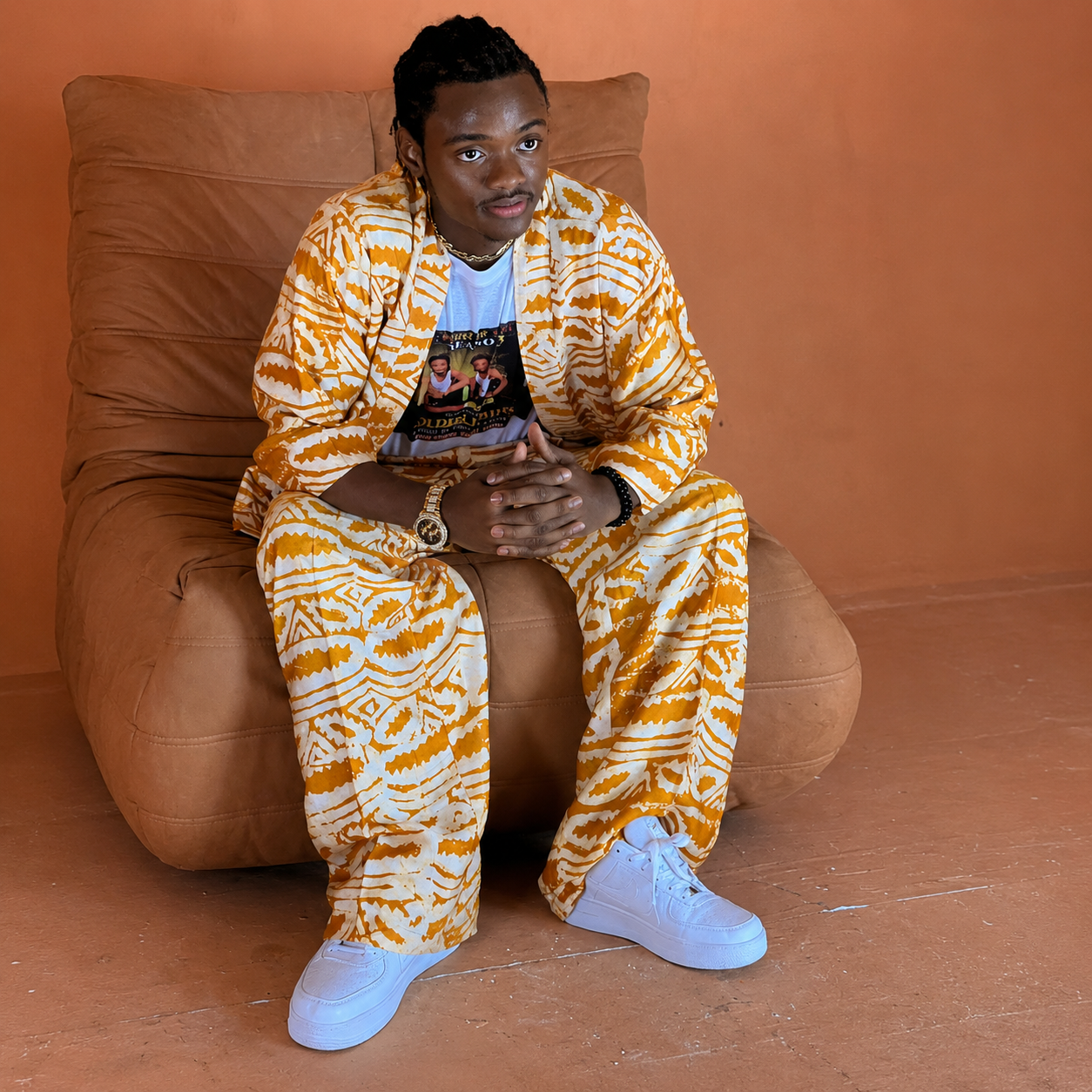 Jacob Sesay seated on a tan couch in a gold-and-white traditional outfit, square portrait